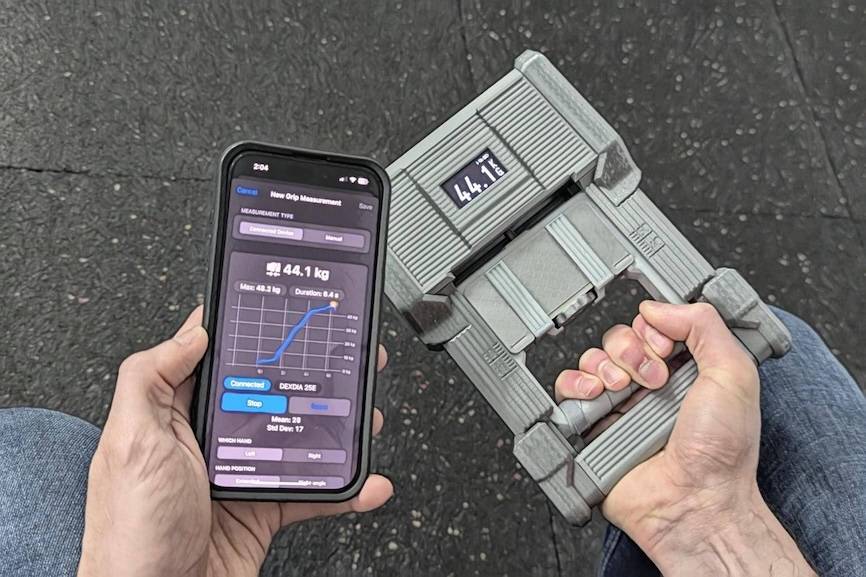 Measuring grip strength of one hand while showing the GripMeter app with the progress of the measurement in the other hand